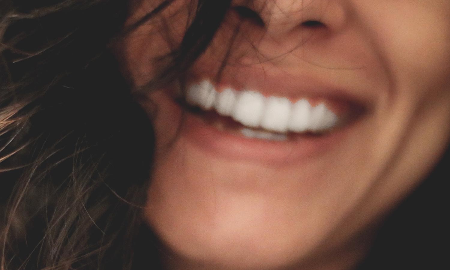 AirFlow jet polishing patient with brown hair smiling and showing bright, white teeth