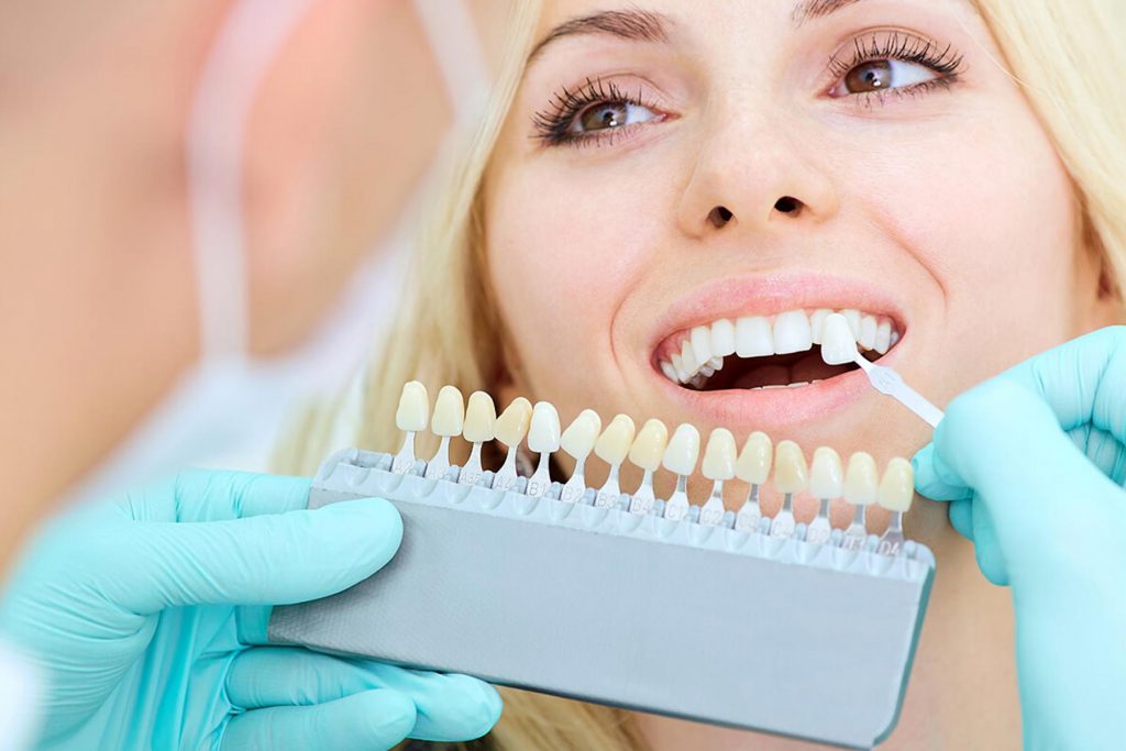 Patient smiling and looking at dentist whilst they shade match their teeth for bespoke veneers