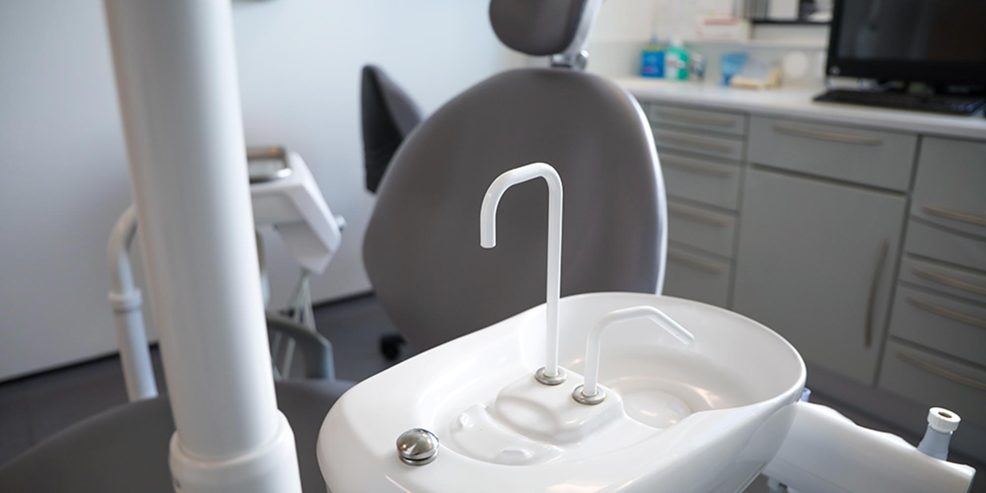 grey dental chair in background of close up of rinsing sink in treatment room