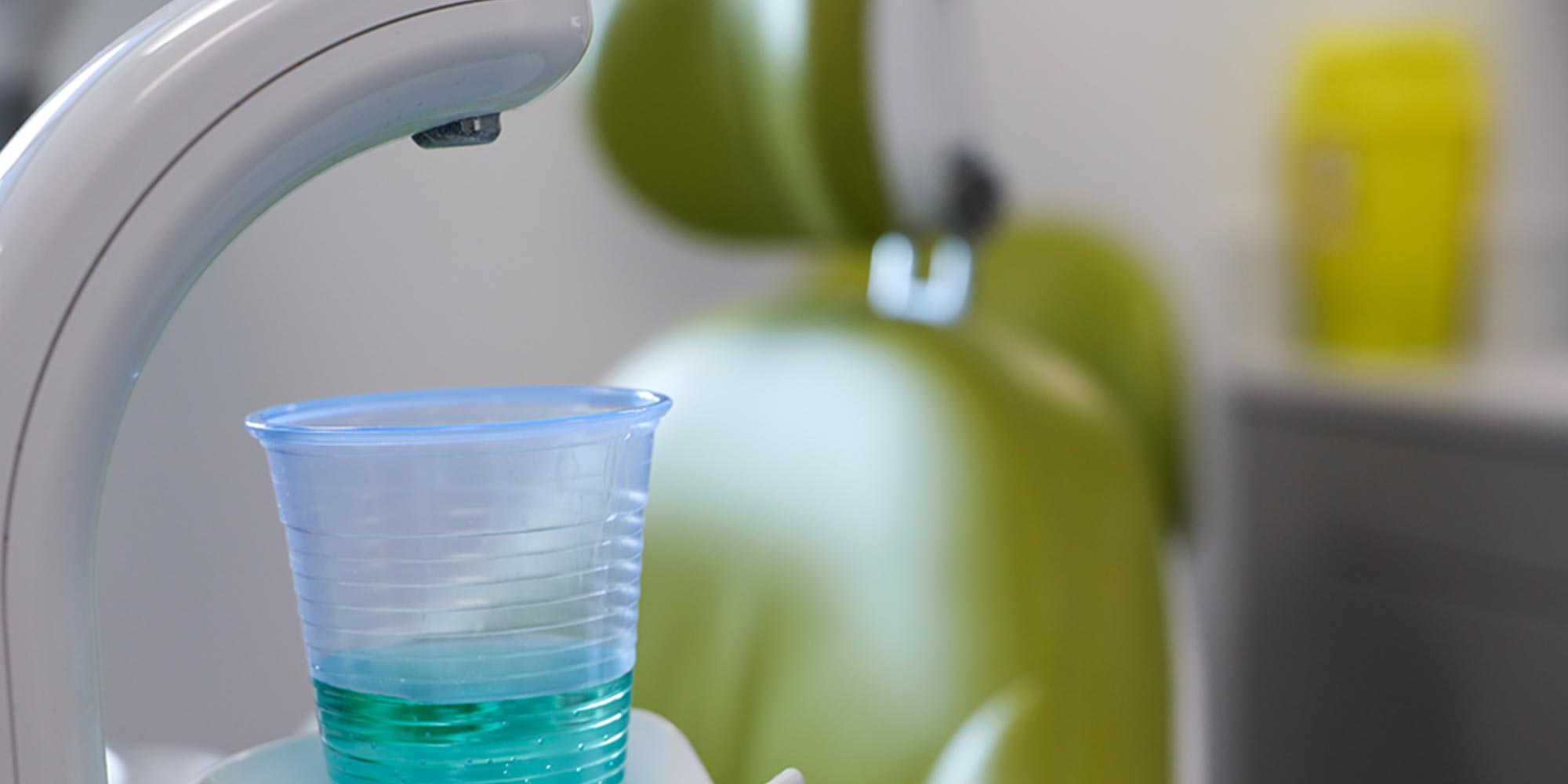 close up of disposable rinsing cup with green dental chair in the background